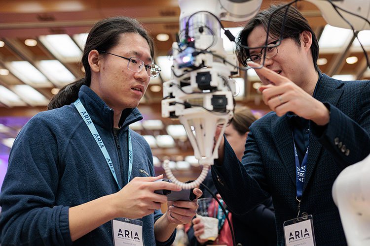 One student demonstrates how a continuum robot works while the other student holds a controller in his hand at the 2024 Applied Research in Action (ARIA) showcase.